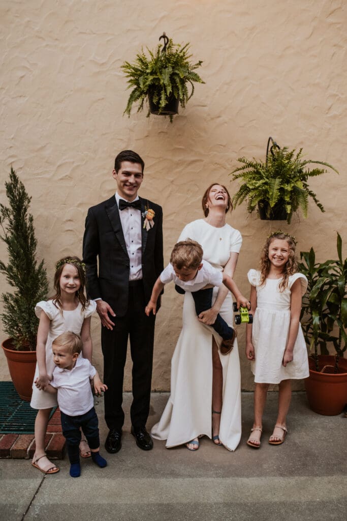 bride and groom with flower girls and ring bearers with the bride trying to hold the unruly ring bearer and she is laughing