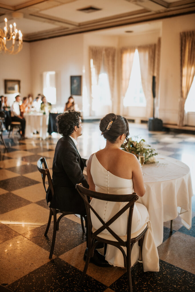 bride and groom sitting at a table listening to speeches