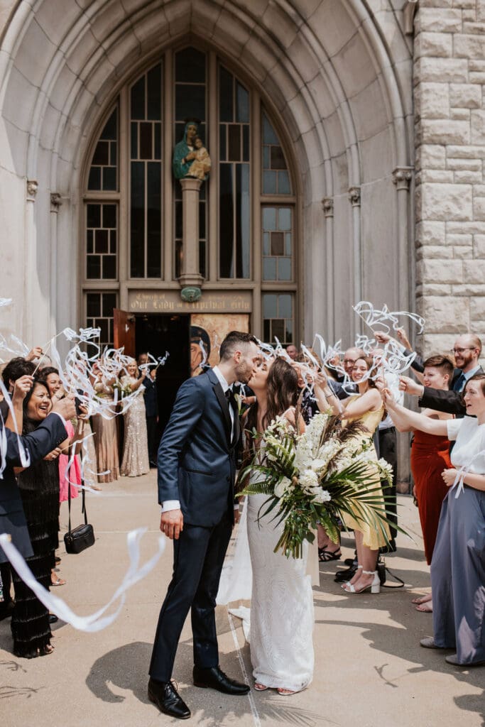 Wedding guests waving ribbon wands as a Catholic couple exits their parish