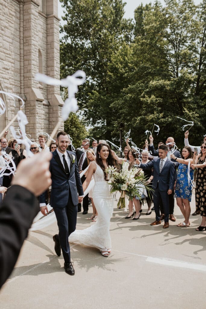 Wedding guests waving ribbon wands as a Catholic couple exits their parish
