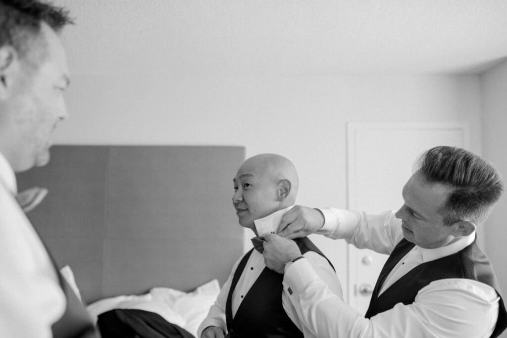 groomsmen helping a groom put his bowtie on
