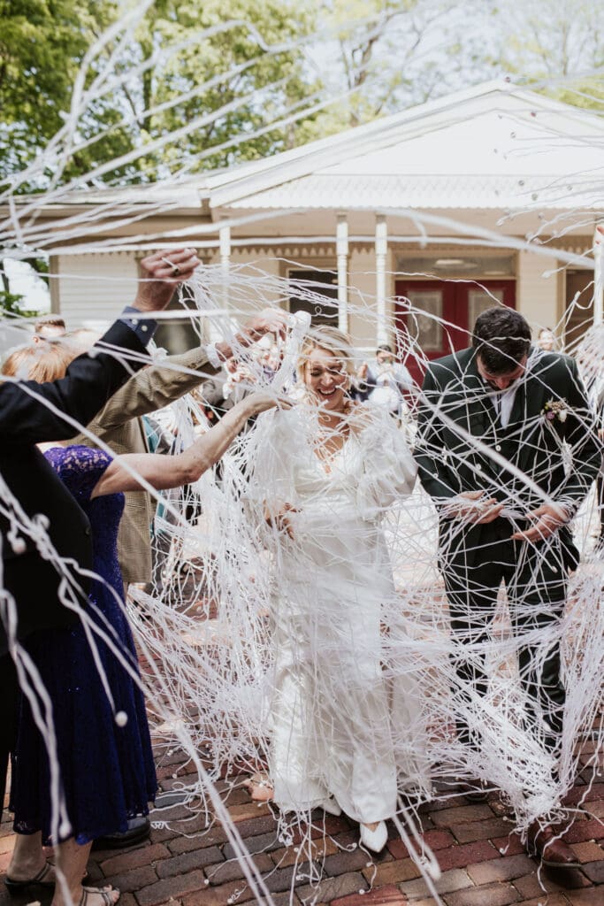 Wedding guests waving streamers as a joyful couple exits the church