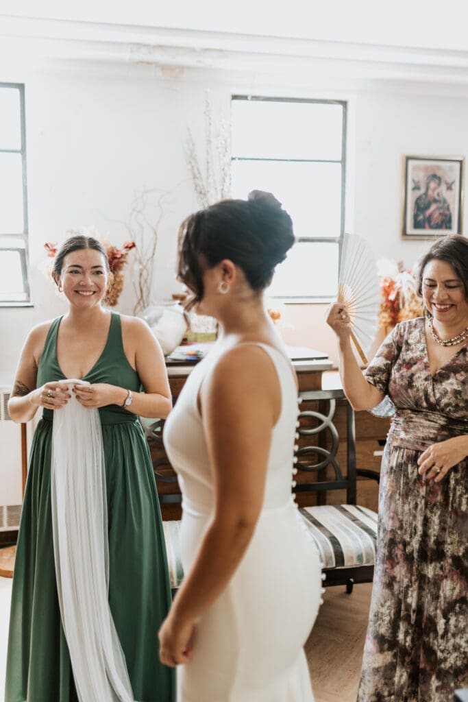 Bride being looked at lovingly by her maid of honor and mother before the ceremony at Gesu Catholic Church