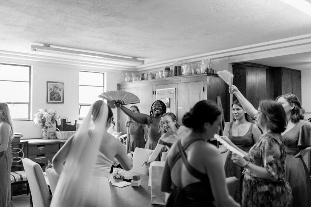 Bride during getting ready moments with her bridesmaids fanning her at Gesu Catholic Church in Detroit Michigan