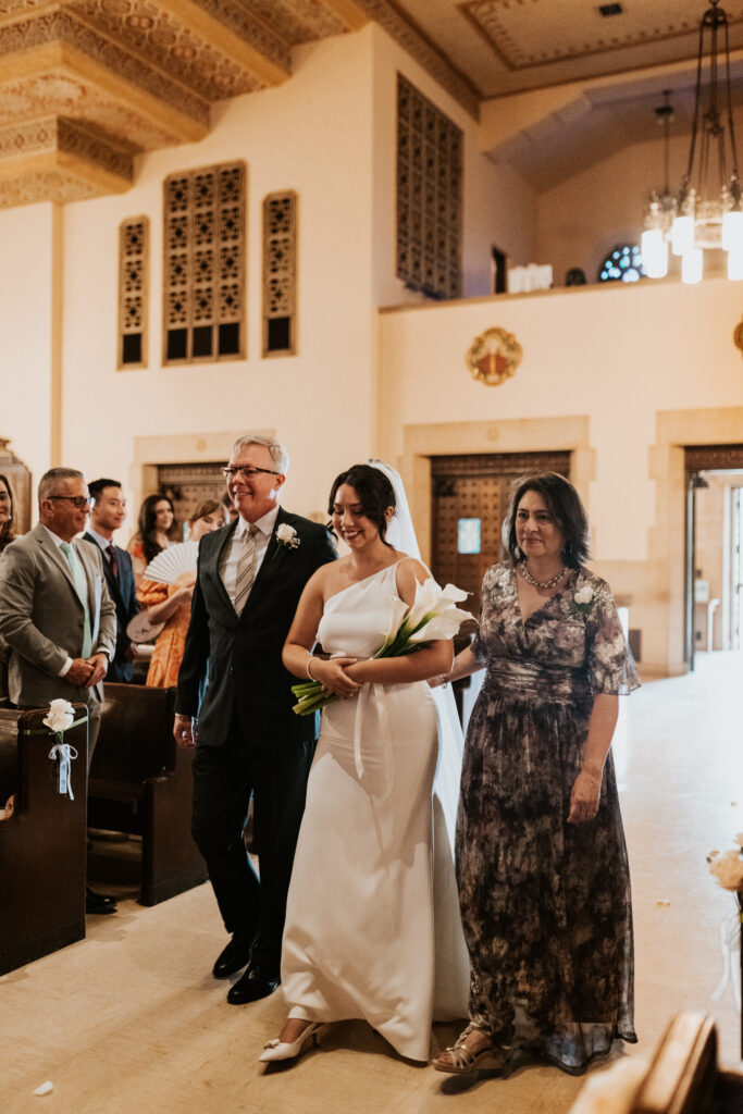 Bride being walked down the aisle with her parents in Gesu Catholic Church in Detroit Michigan