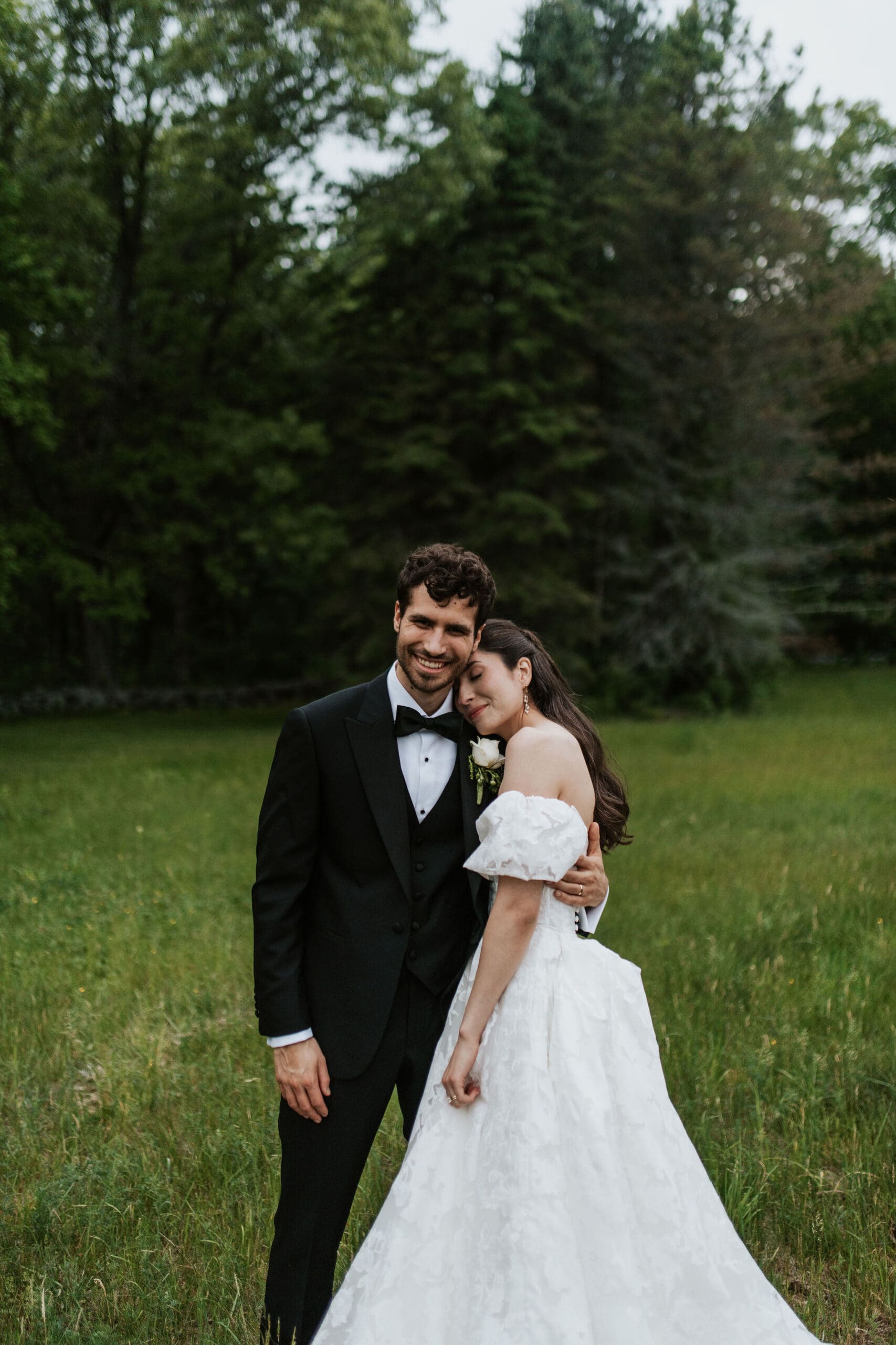 A bride leaning against her husband in the field during their faith-based wedding in boston
