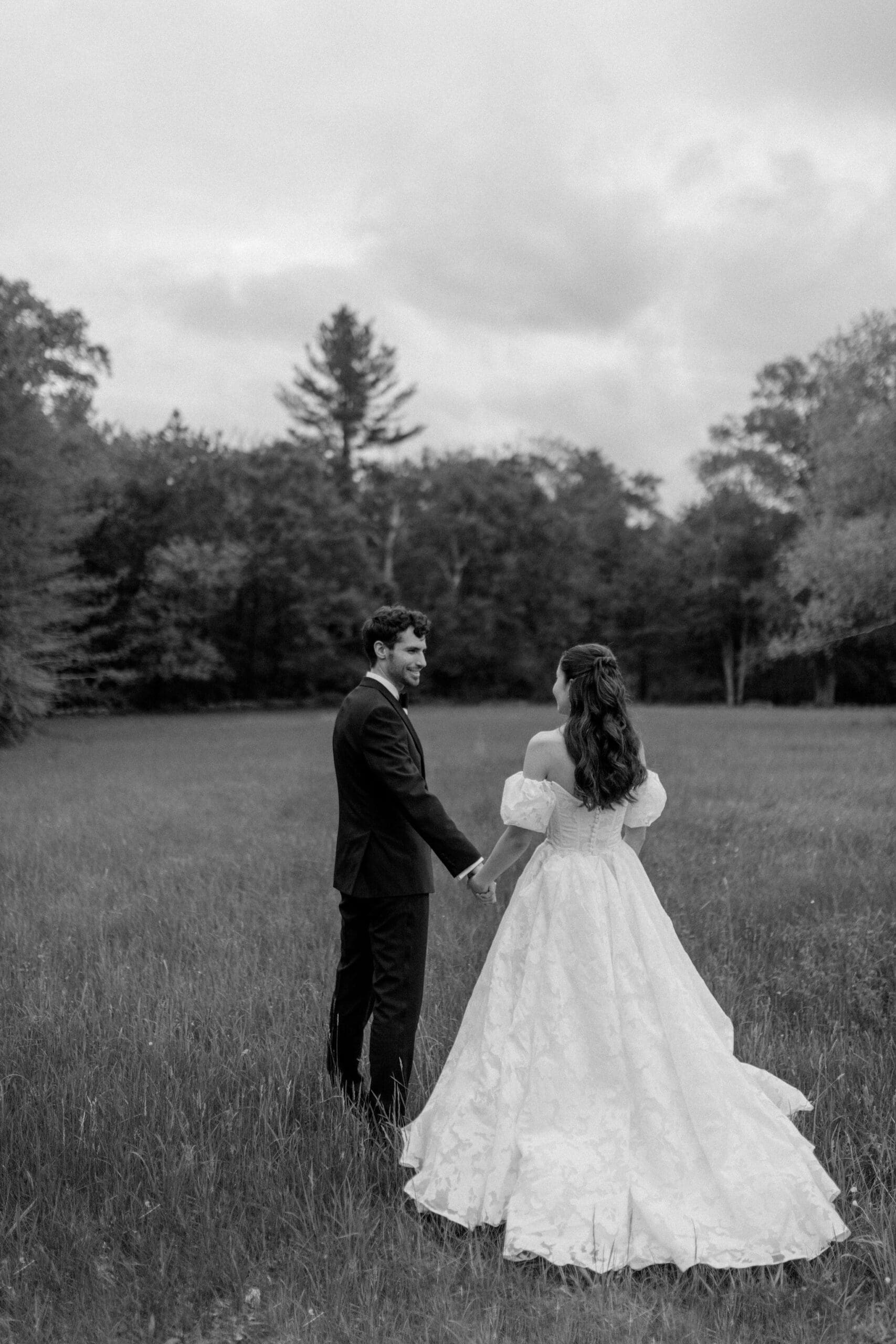 a bride looking lovingly at her new groom in a field while holding hands during their boston wedding