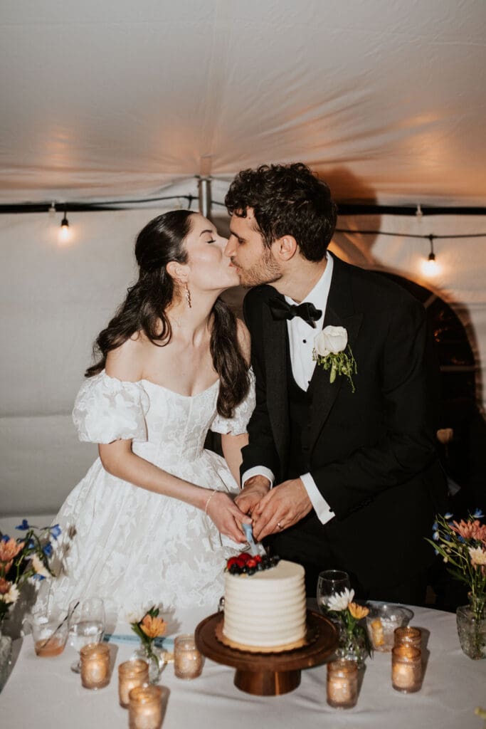 a bride and groom kiss as they cut their wedding cake