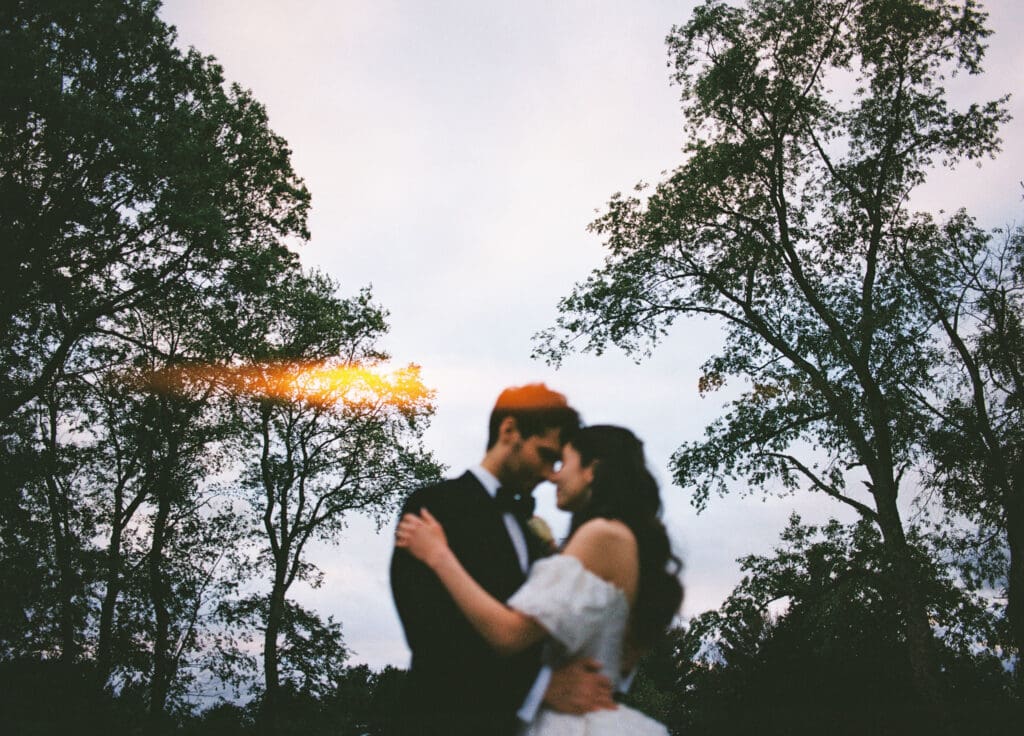 a film photo of a couple touching foreheads in an embrace outdoors in Boston with a light flare on their wedding day