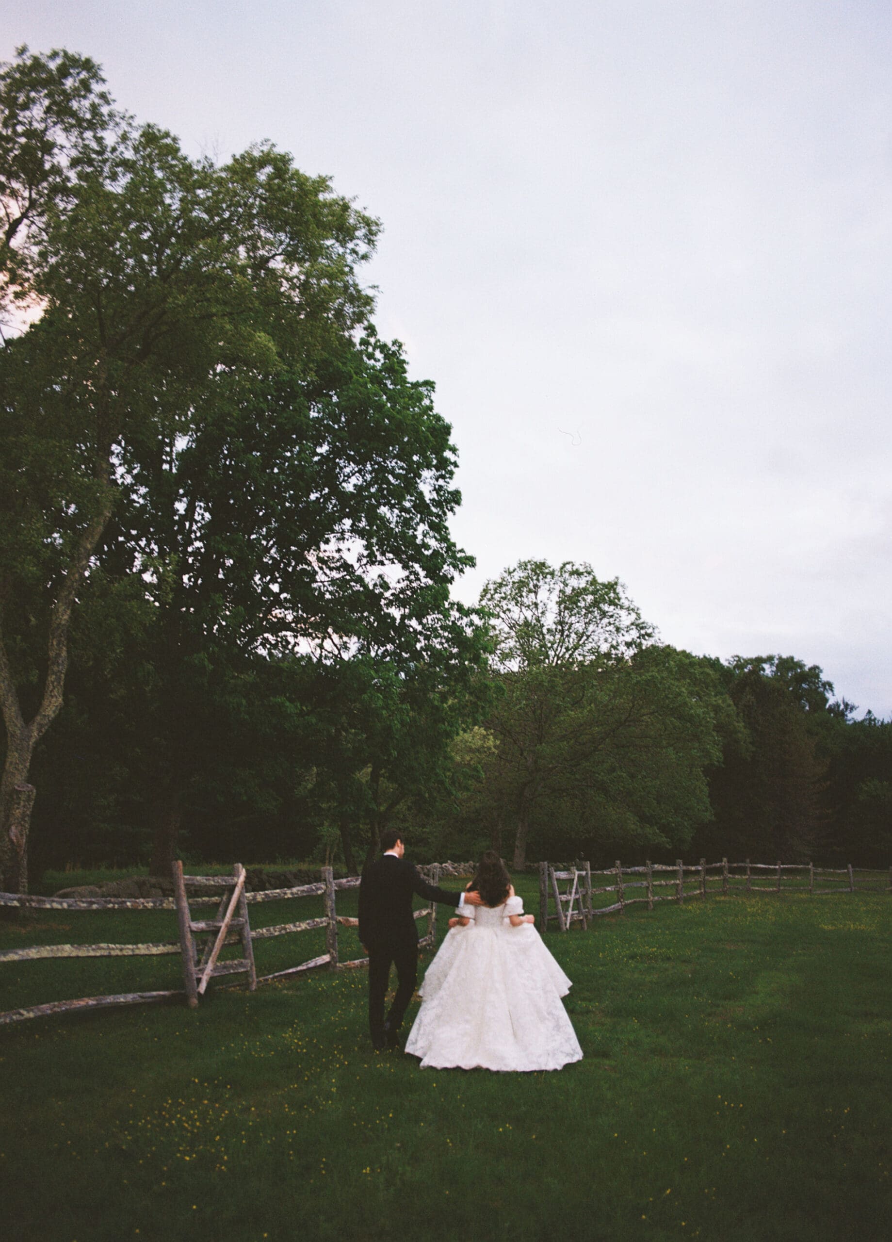 A dreamy film photo of a newly married couple walking away from the camera in a field