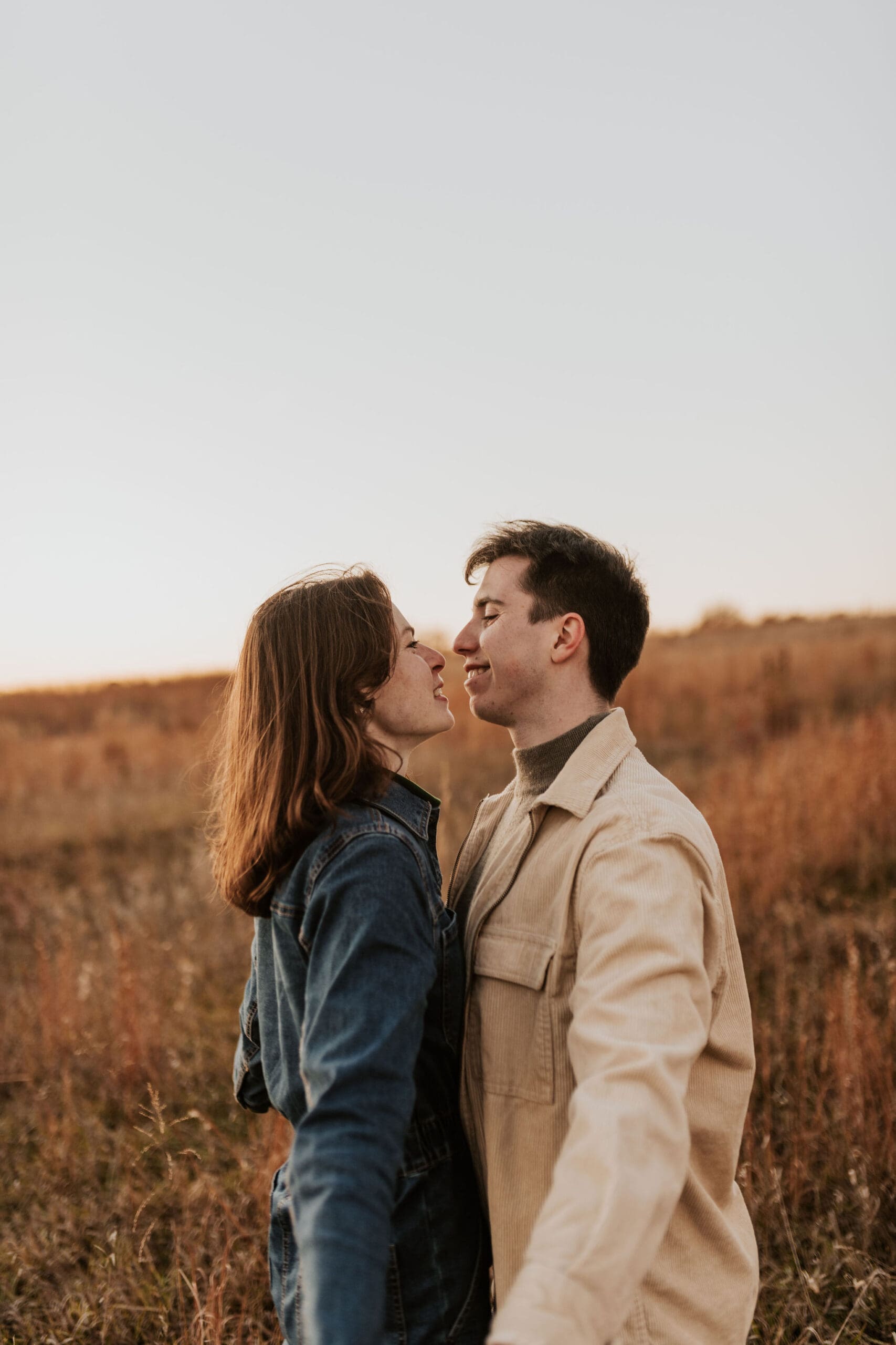 Engaged couple smiling at each other in the middle of a fall field