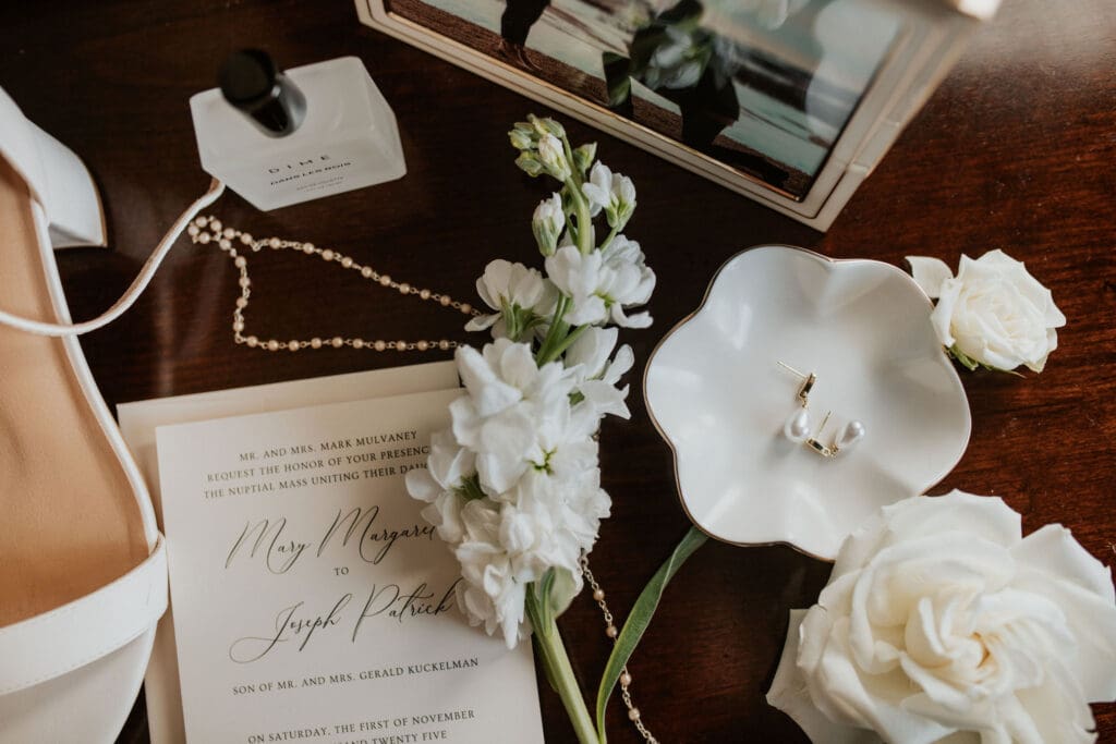 Elegant flat lay of bride’s wedding details including invitation suite, jewelry, and perfume bottle for fall wedding in Atchison KS