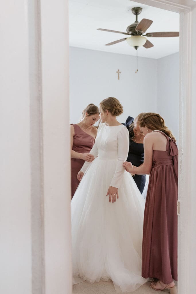 Bridesmaids and mother of the bride helping bride with gown near St. Benedict’s Parish Atchison