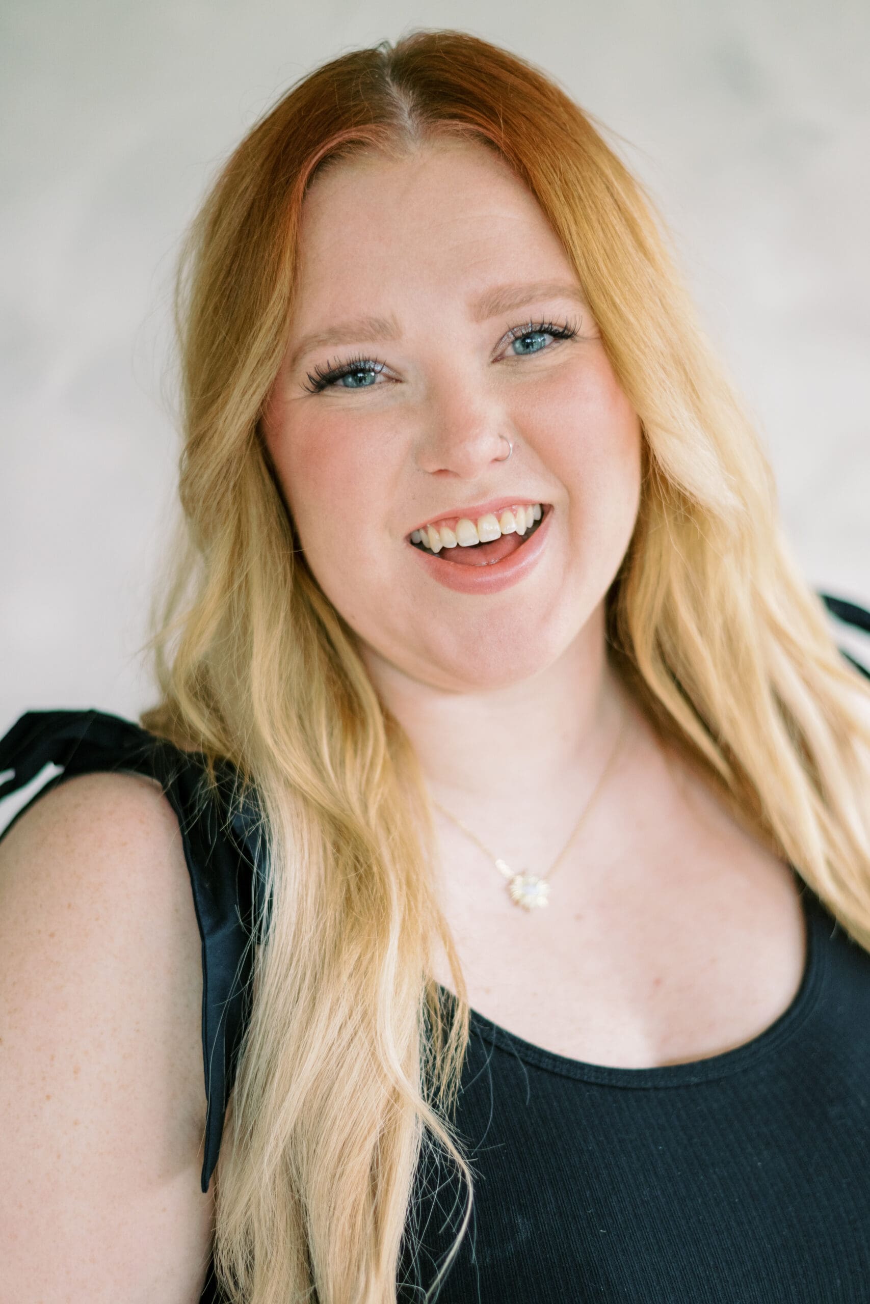 Bailey, owner of Bailey Rose Makeup Artistry, smiling in a natural light headshot with soft glam makeup and loose waves