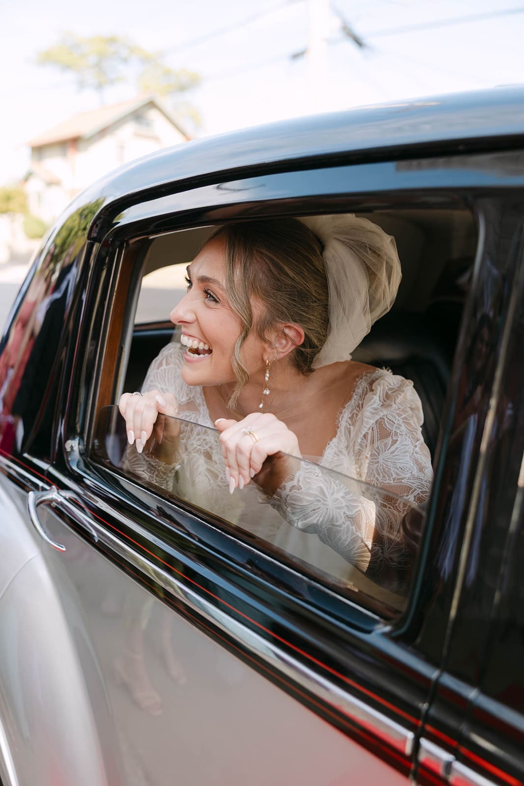 Bride smiling out the window of a vintage car with soft romantic makeup and an elegant low bun