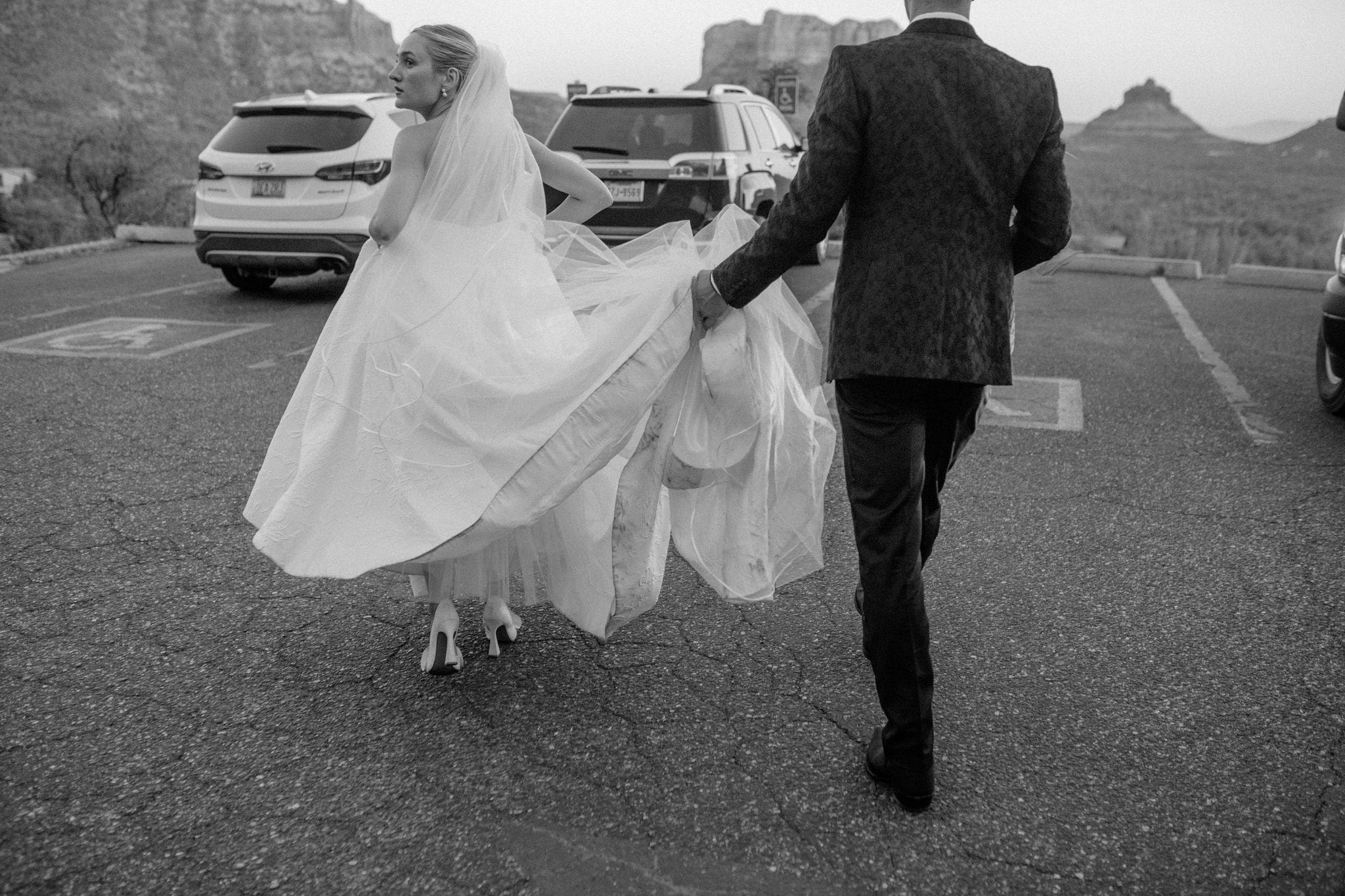 Candid wedding photo of groom holding bride's dress after their ceremony