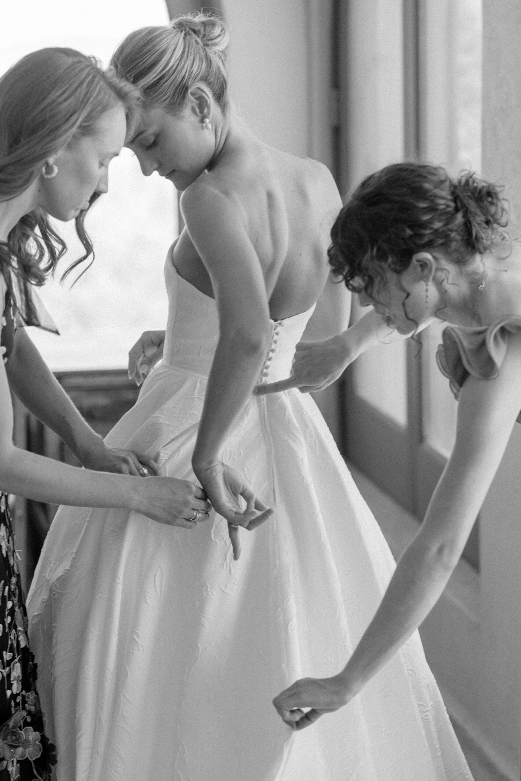Bridesmaids helping button wedding gown during a Catholic wedding morning