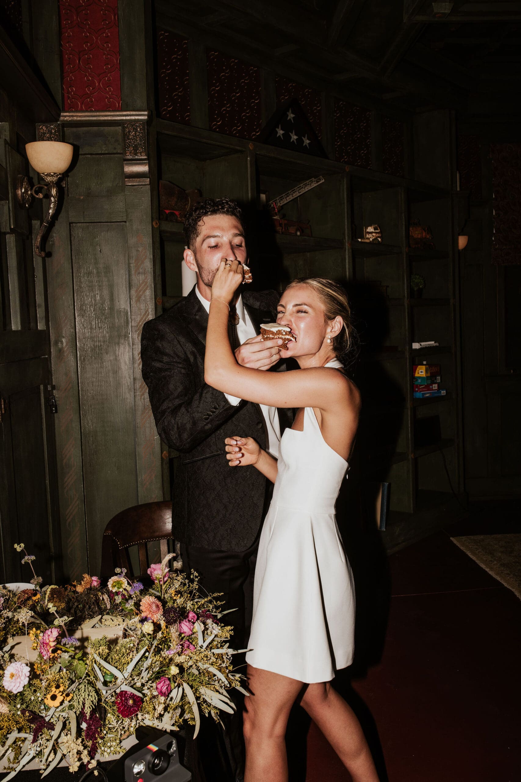 Playful cake cutting moment at Arizona Catholic wedding reception with colorful florals