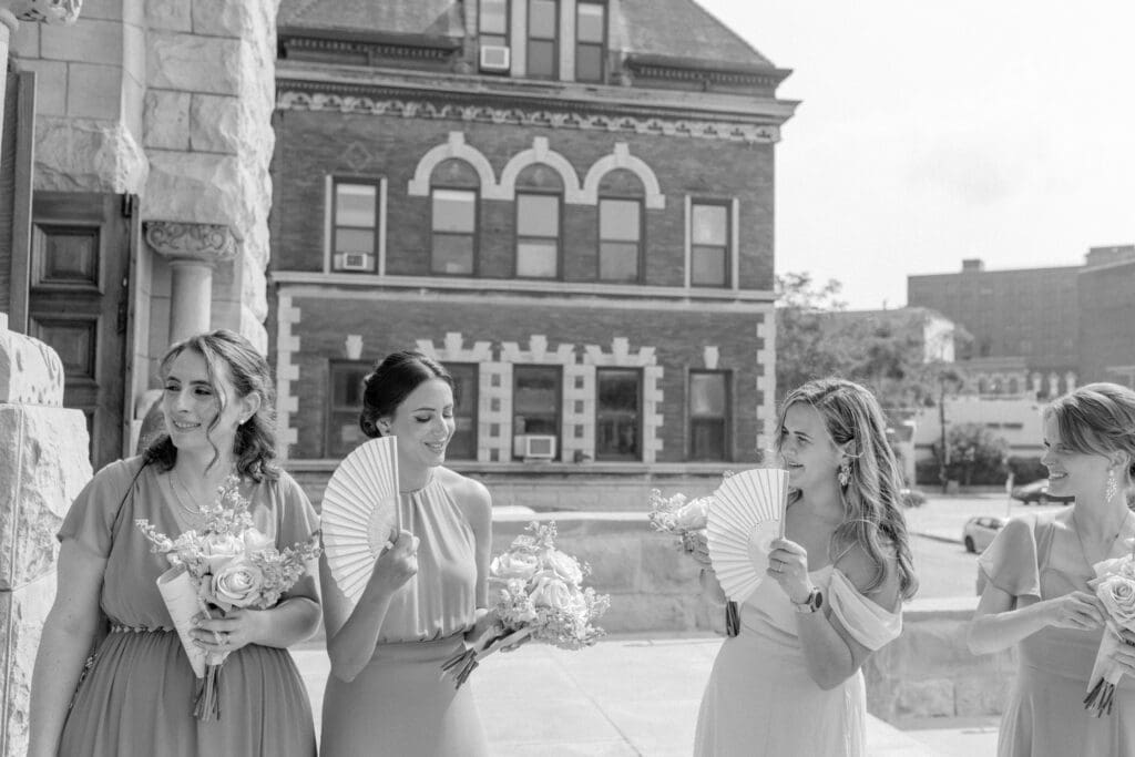Bridesmaids waiting outside for the bride and groom exit while fanning themselves outside the church of Saint John Cantius in Chicago