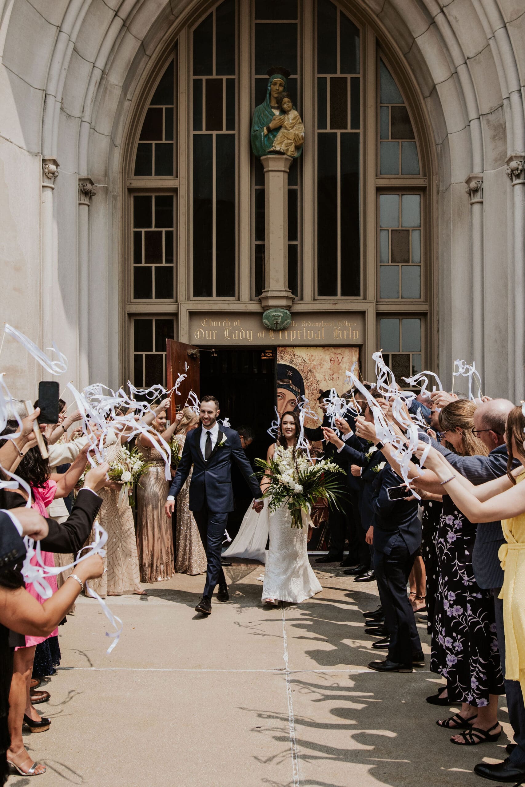 joyful catholic church wedding exit outside Our Lady of Perpetual Help with ribbon send off