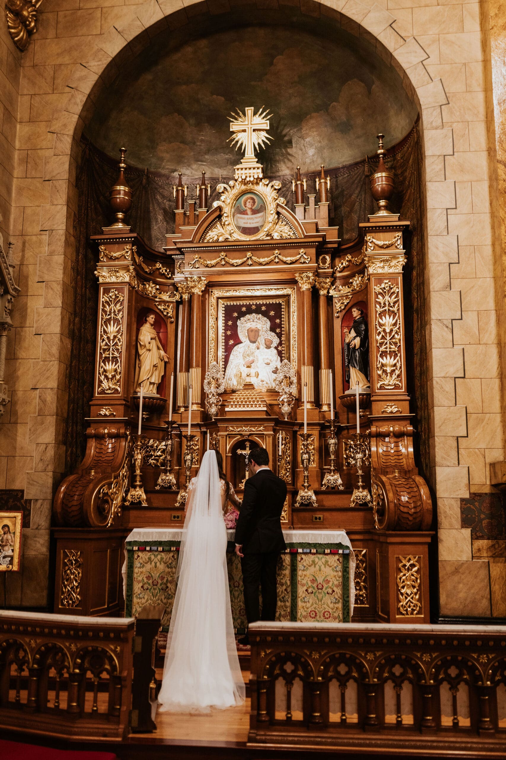 Bride and groom praying together at Marian altar during Saint John Cantius Chicago wedding ceremony.