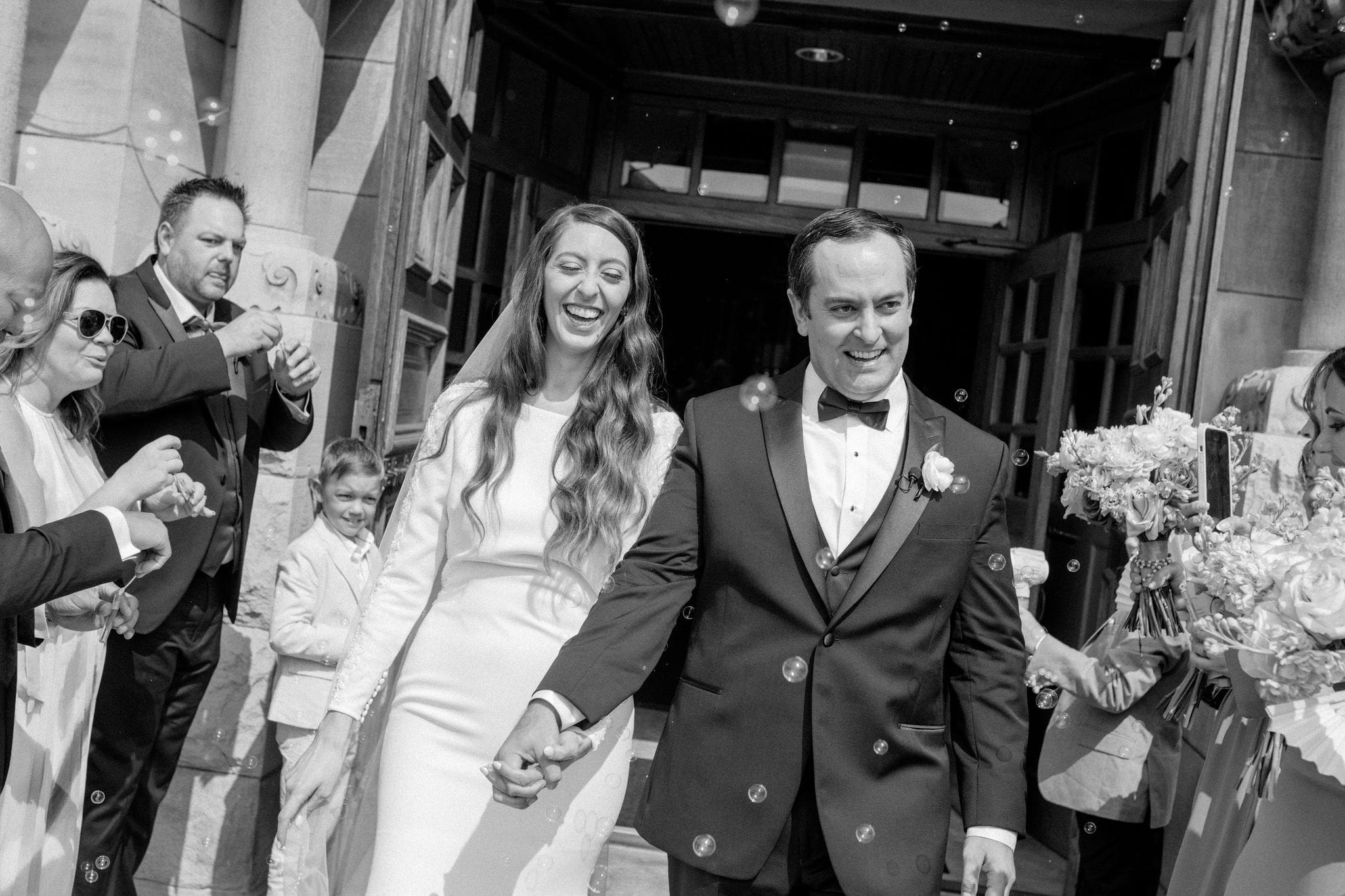Newly married couple exiting Saint John Cantius Chicago church surrounded by guests blowing bubbles.