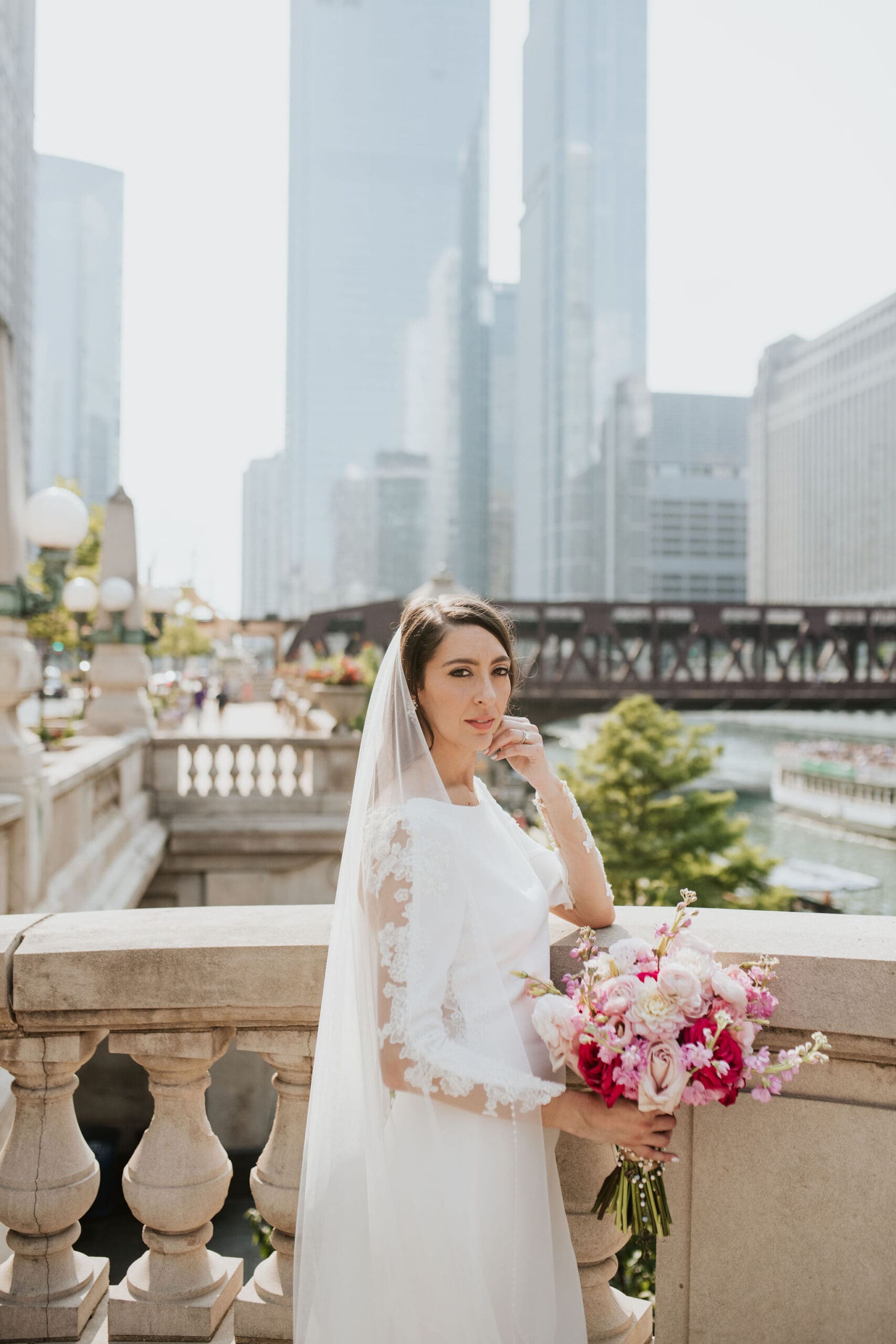 Bride holding pink bouquet with Chicago skyline and riverwalk behind her during wedding portraits.