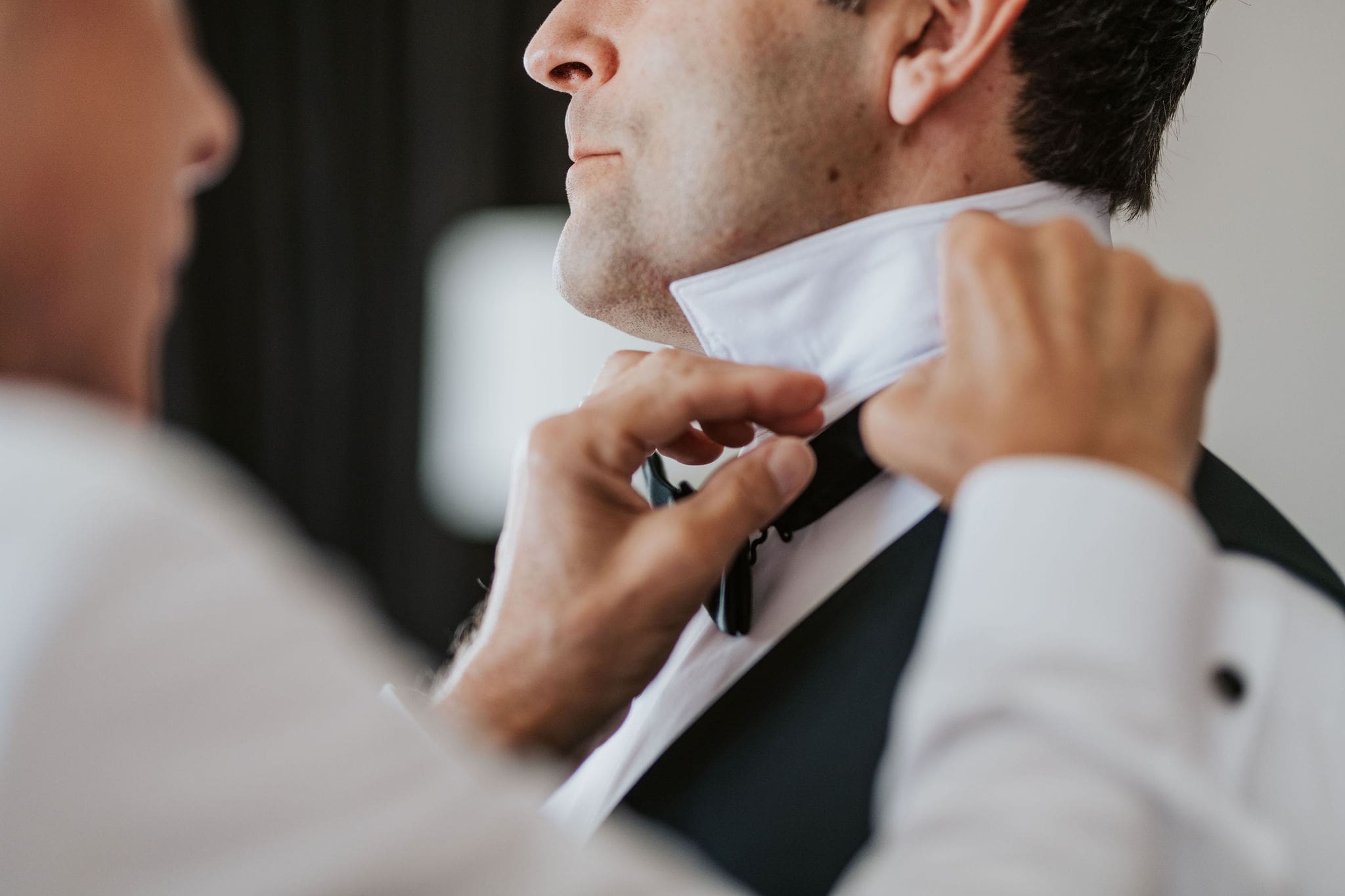 Groom adjusting his tuxedo collar during wedding morning preparations.