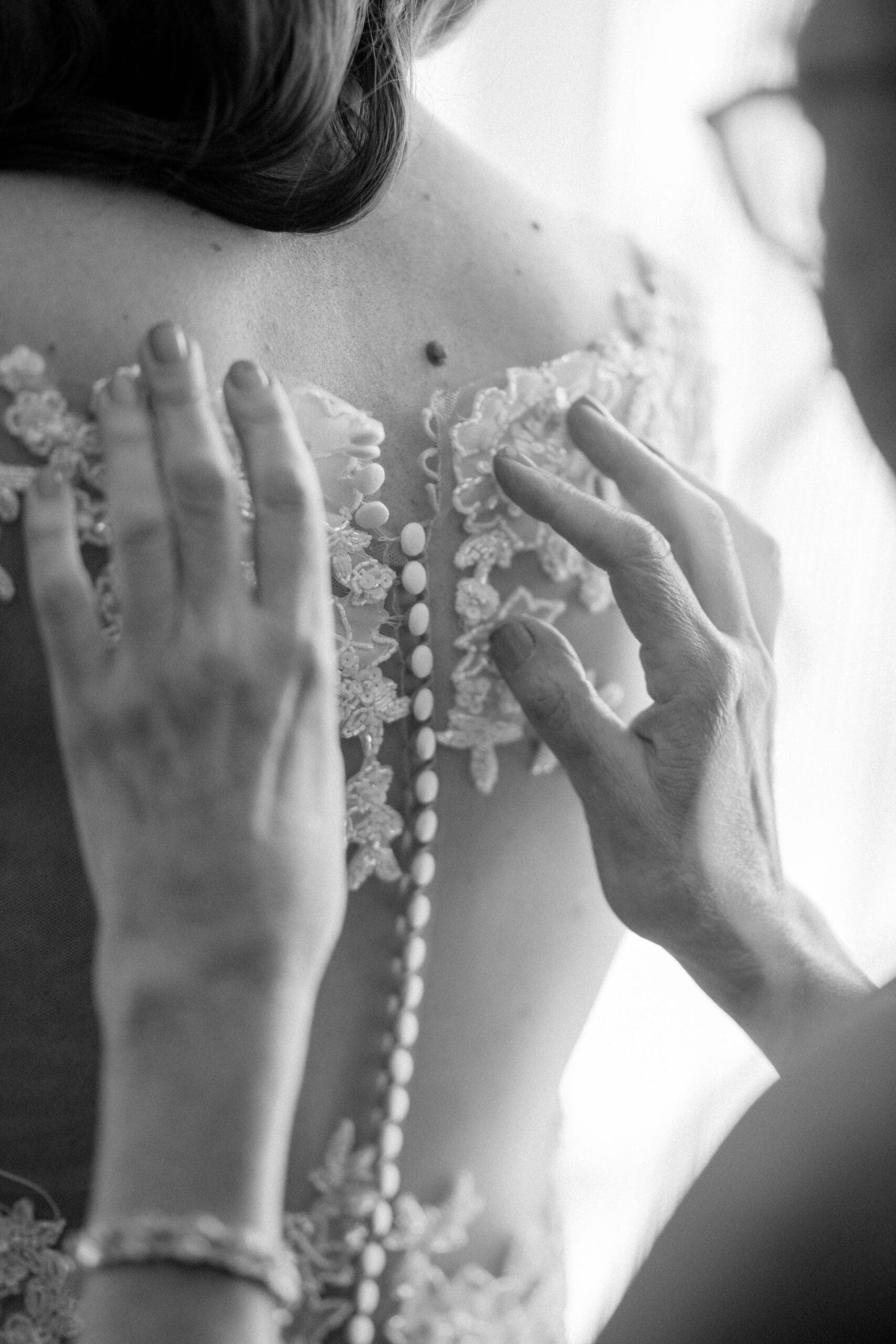 Close up of hands fastening buttons on lace wedding dress during bridal preparations.