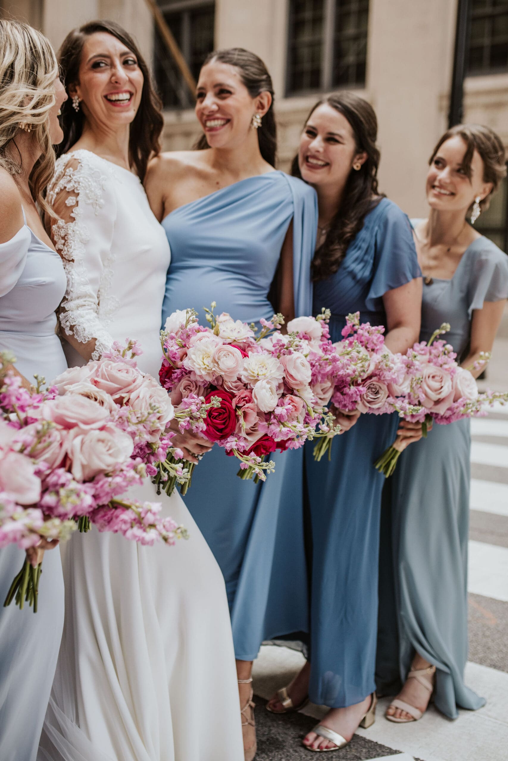 Bride and bridesmaids holding pink floral bouquets and wearing blue dresses during Chicago wedding portraits.
