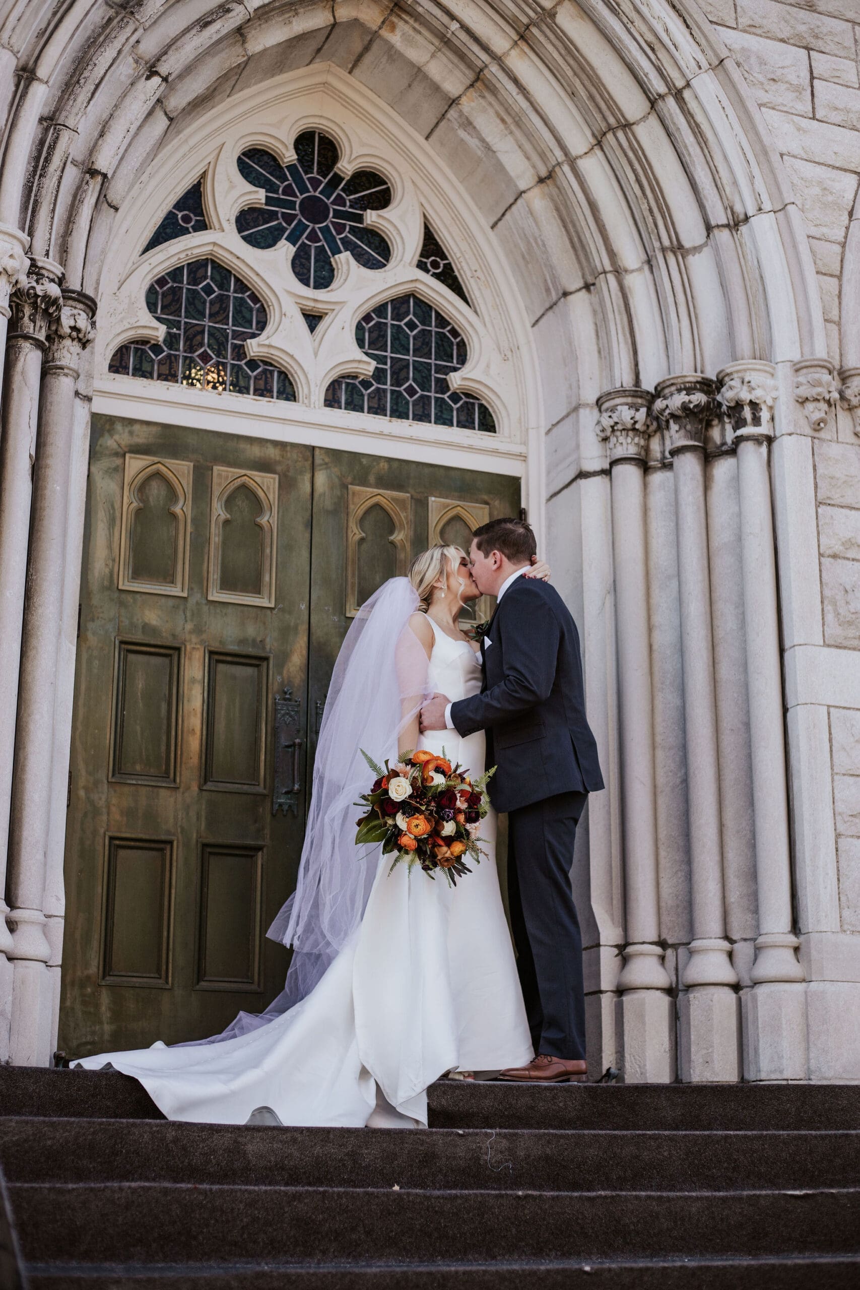Bride and groom sharing a kiss on cathedral steps after their Kansas City Catholic church wedding ceremony