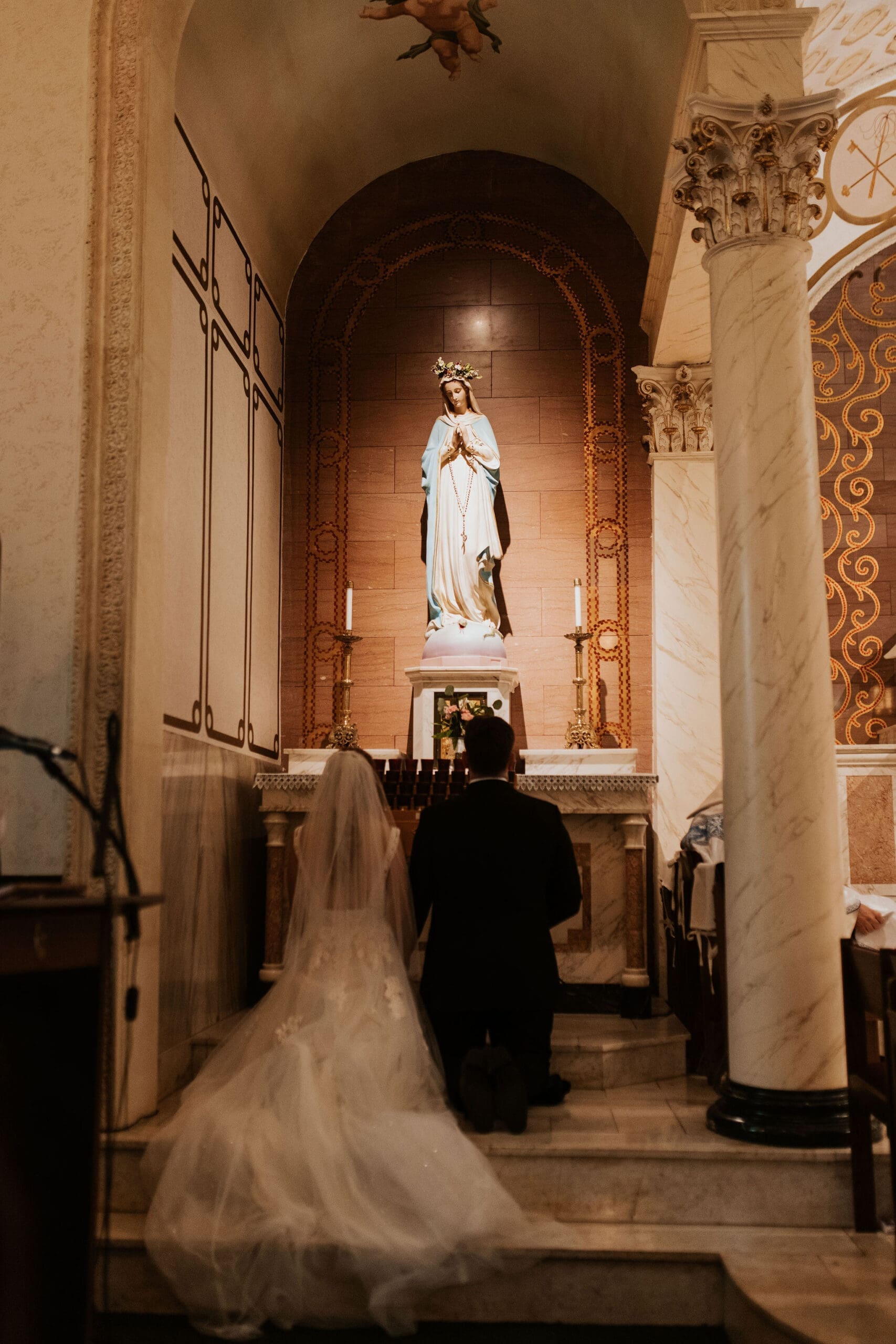 Bride And Groom kneeling before the mary statue during their catholic wedding ceremony at holy trinity catholic church in lenexa kansas