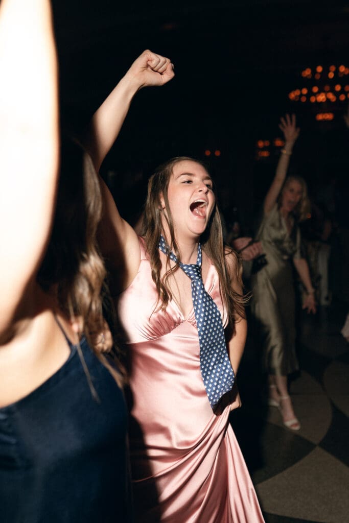 A high-energy color photo of wedding guests dancing at the Hilton President Kansas City reception, captured with direct flash. The lighting creates a vibrant, editorial party atmosphere with sharp details and deep shadows.