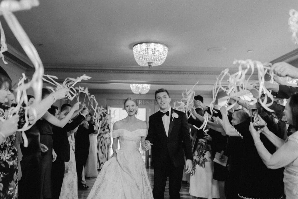 A timeless black and white photograph of the newlyweds inside the historic golden elevator at the Hilton President Kansas City. The bride and groom are sharing a final joyful look back at their guests as the elevator doors begin to close.