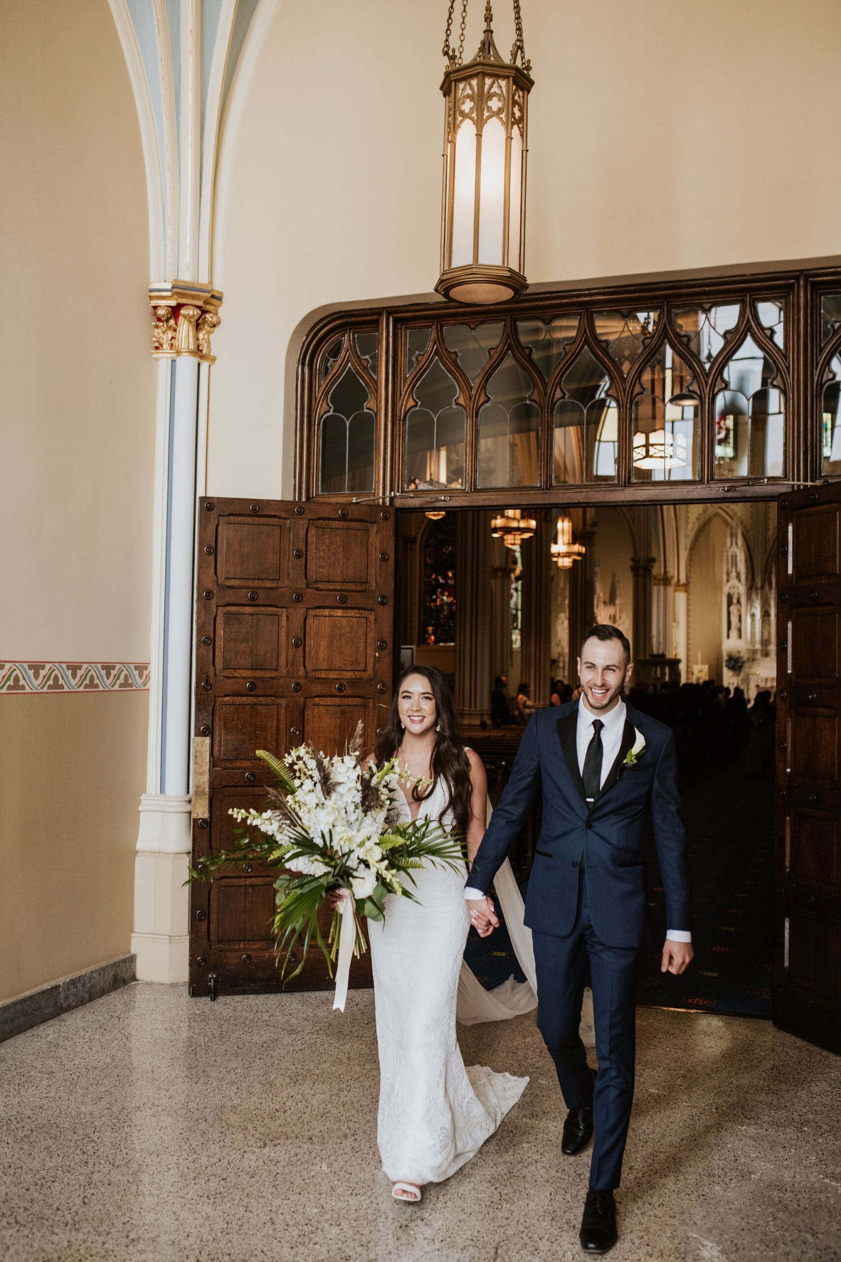 Newly married couple walking through the grand wooden doors after their Catholic wedding ceremony in Kansas City