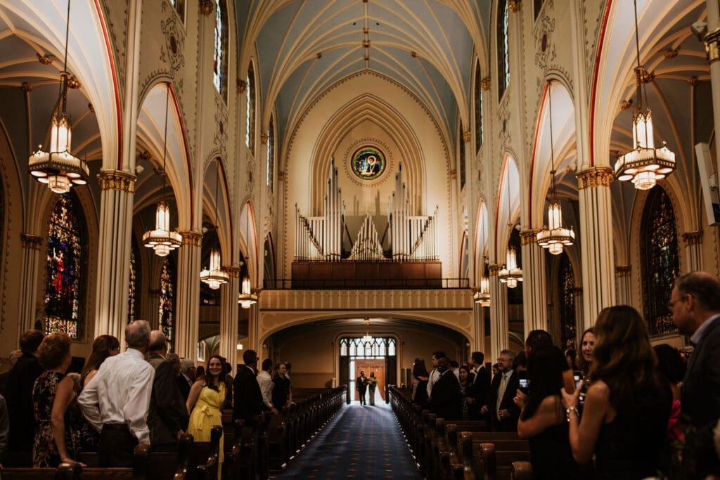 Wide view of guests gathered inside a historic Kansas City Catholic church with vaulted ceilings and glowing stained glass