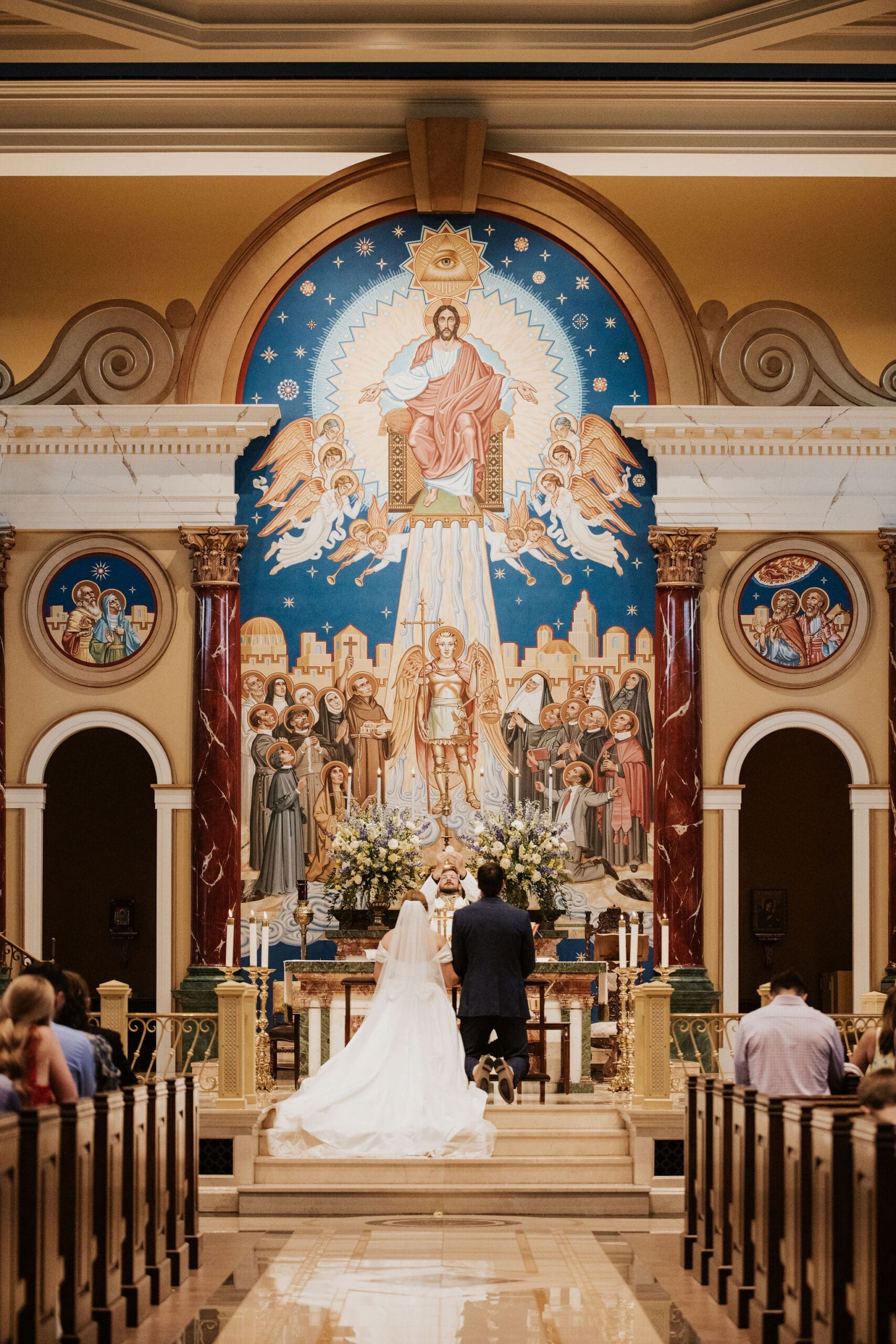 Intimate church wedding ceremony with the bride and groom kneeling at the altar surrounded by elegant architecture and warm candlelight.