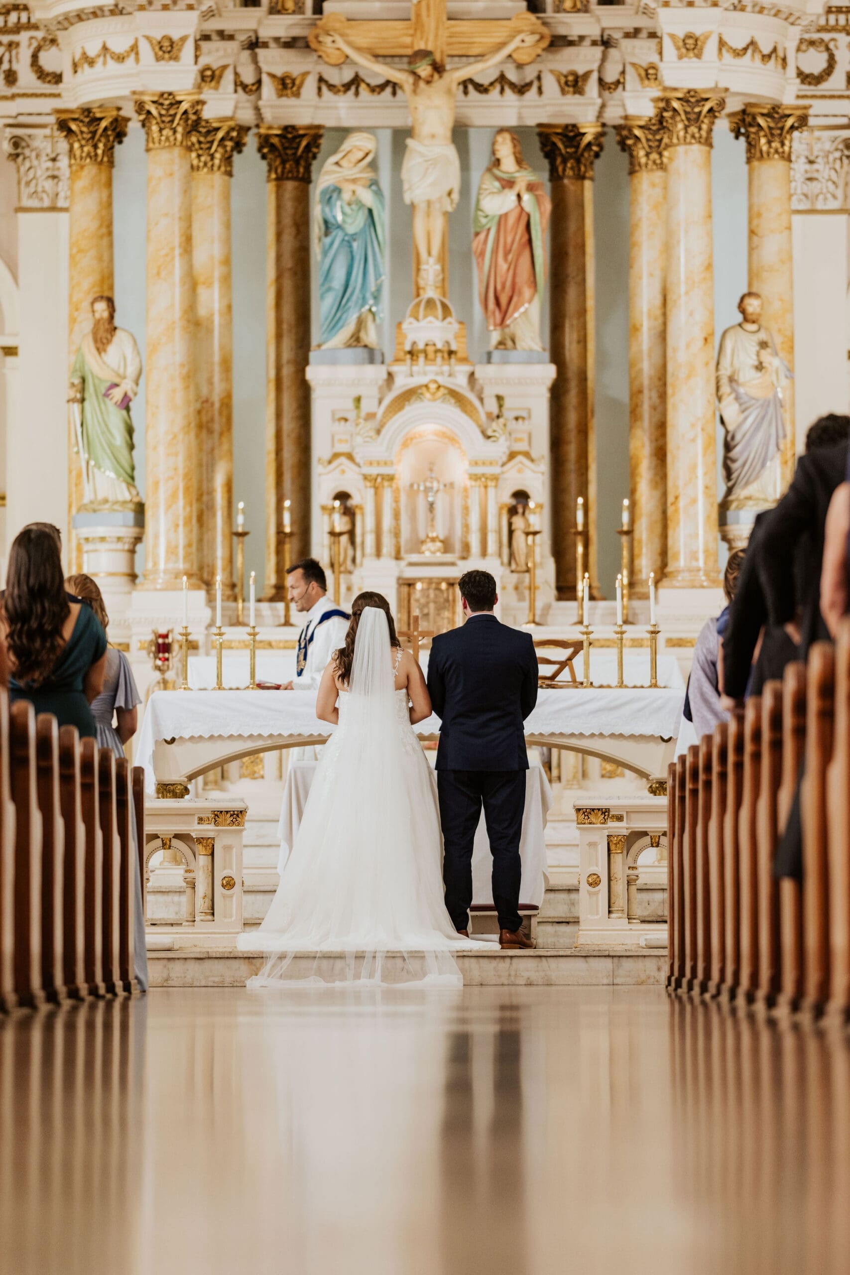 Emotional church wedding ceremony photographed from the aisle with soft light reflecting across the floor and wooden pews.