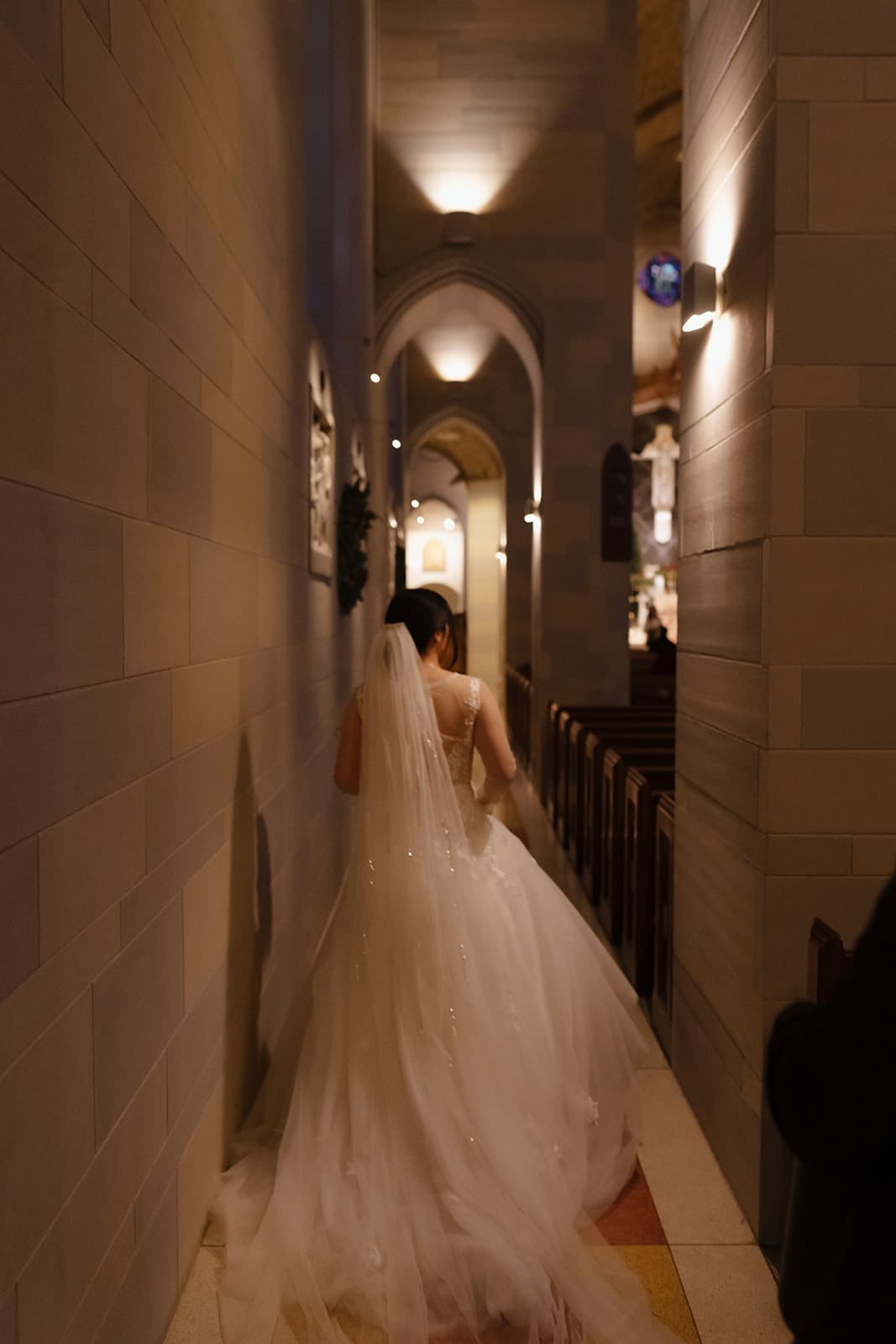 A bride walking through church aisle with long veil and flowing wedding gown