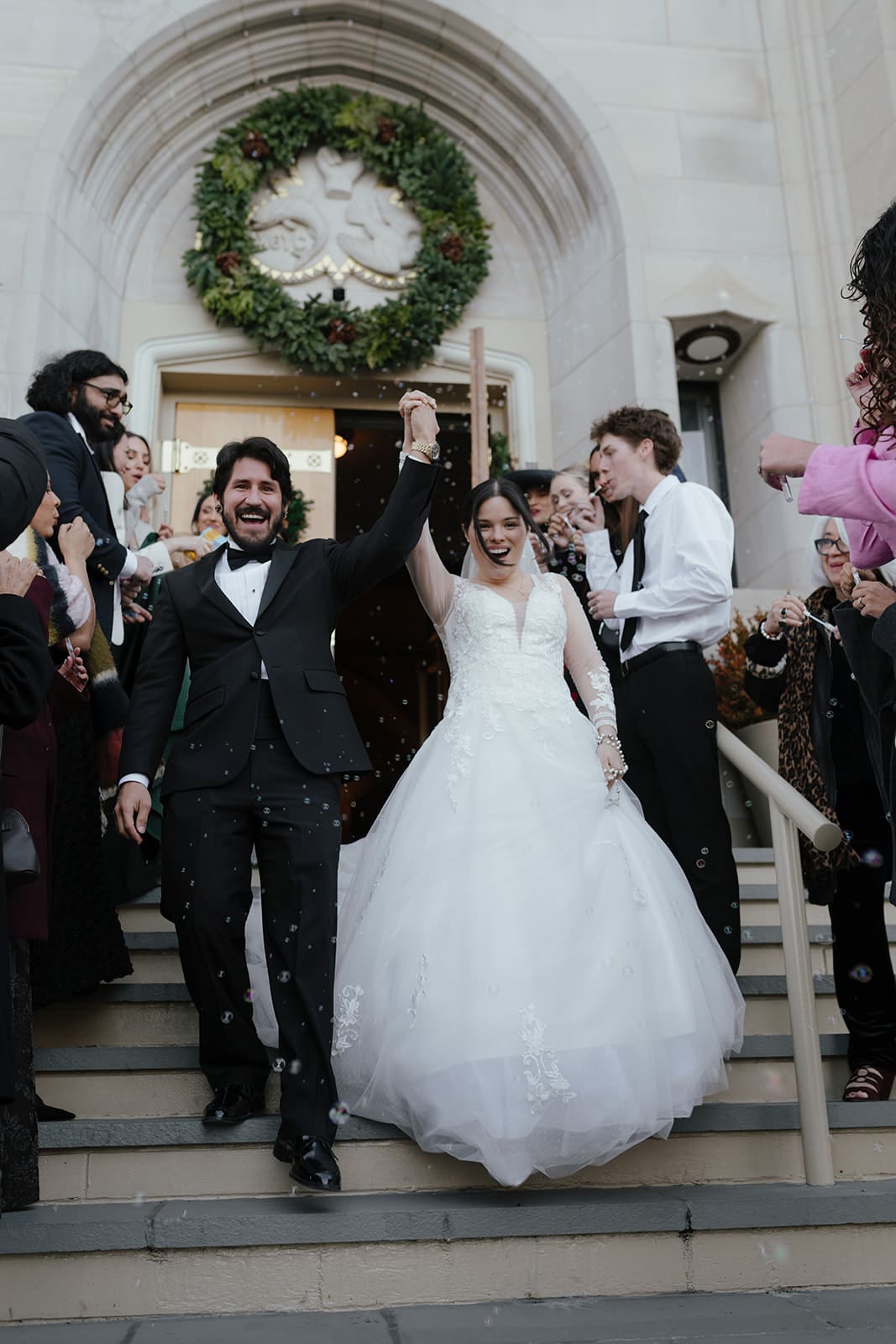 A newlywed couple walking out of church surrounded by guests blowing bubbles