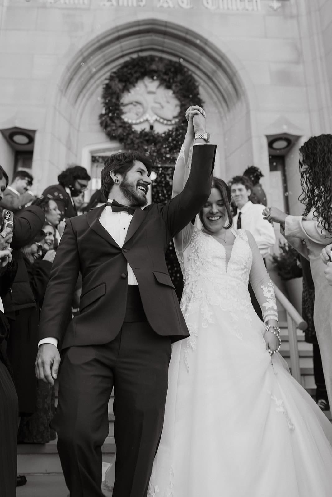 A black and white photo of bride and groom celebrating outside church with guests