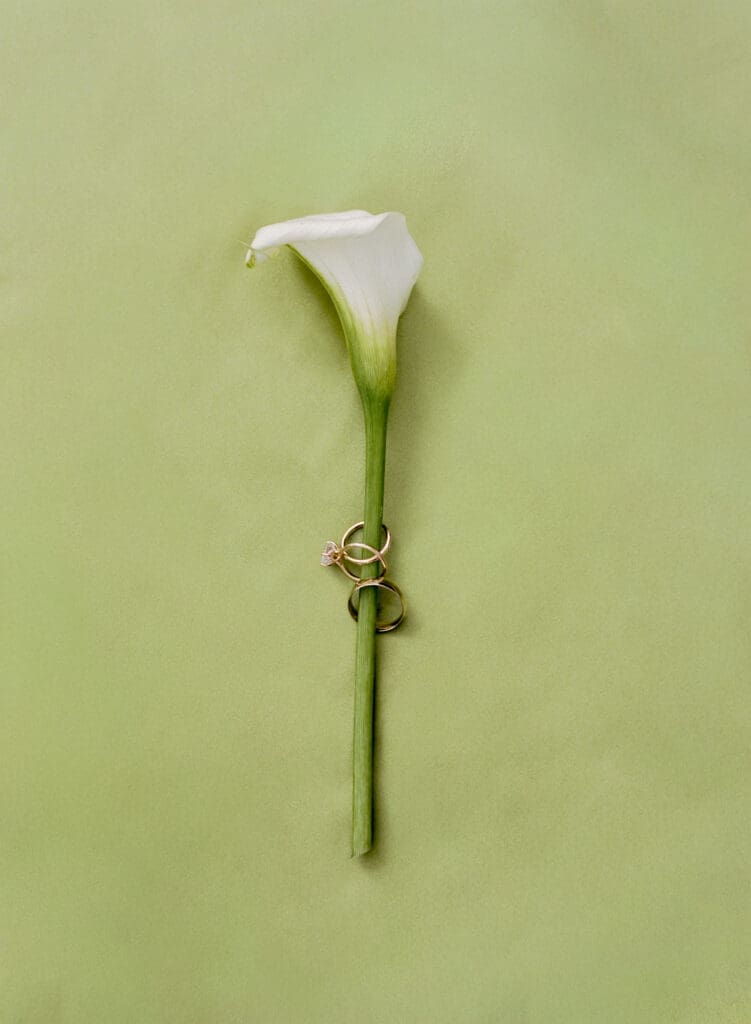 White calla lily boutonniere with wedding rings styled for timeless wedding flat lay inspiration