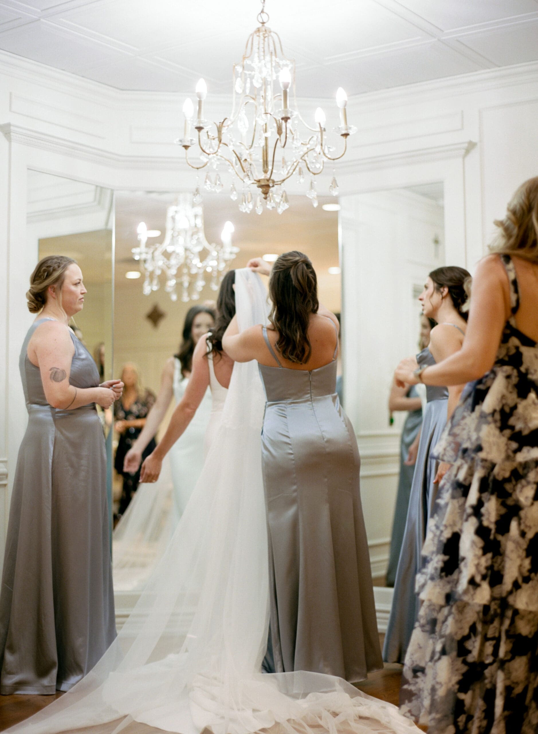 Bridesmaids helping bride with cathedral veil before ceremony in luxury wedding suite