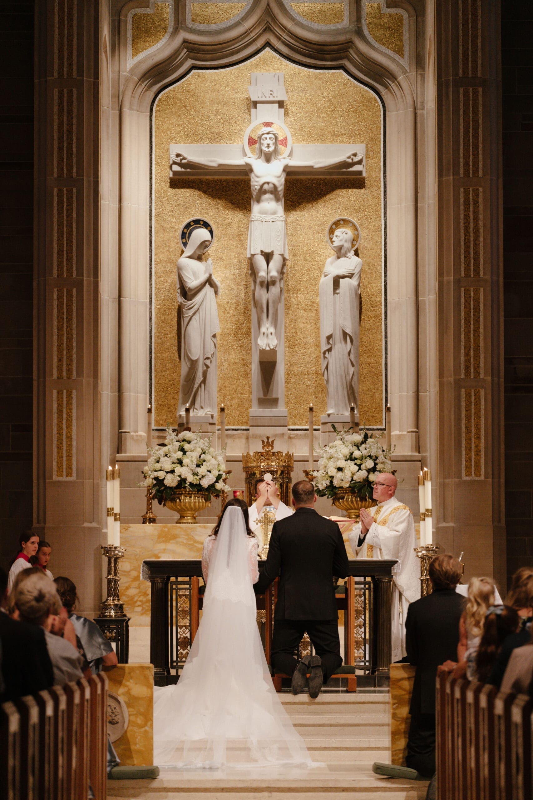 Traditional Catholic wedding ceremony inside ornate cathedral with bride and groom kneeling at altar