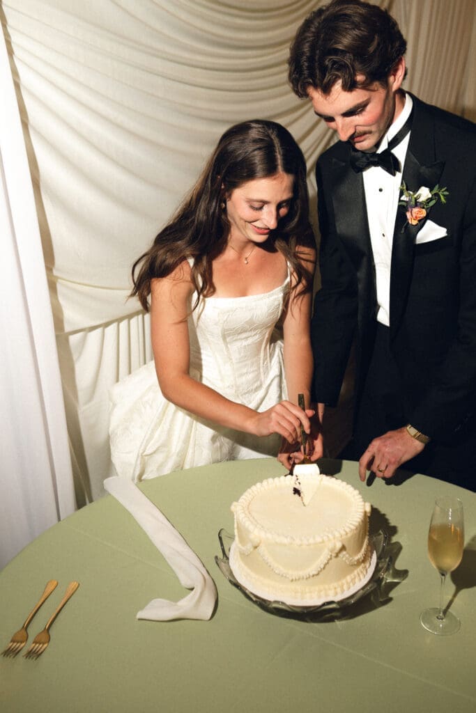 The bride and groom laughing together during their cake cutting ceremony on the grass at Longview Mansion, captured with high-contrast direct flash.