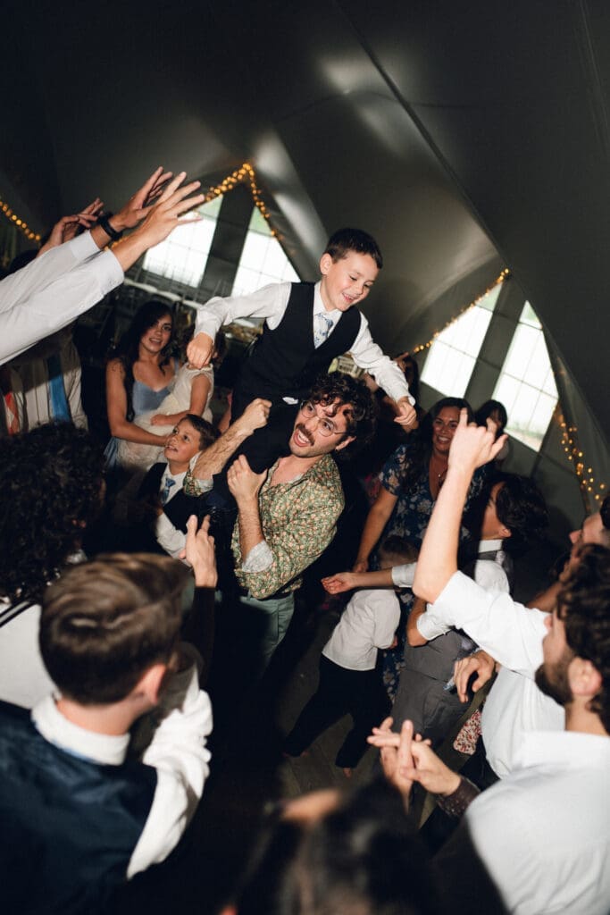 High-energy wedding reception dance floor inside the Longview Mansion Pavilion featuring a guest lifting another guest onto his shoulders.