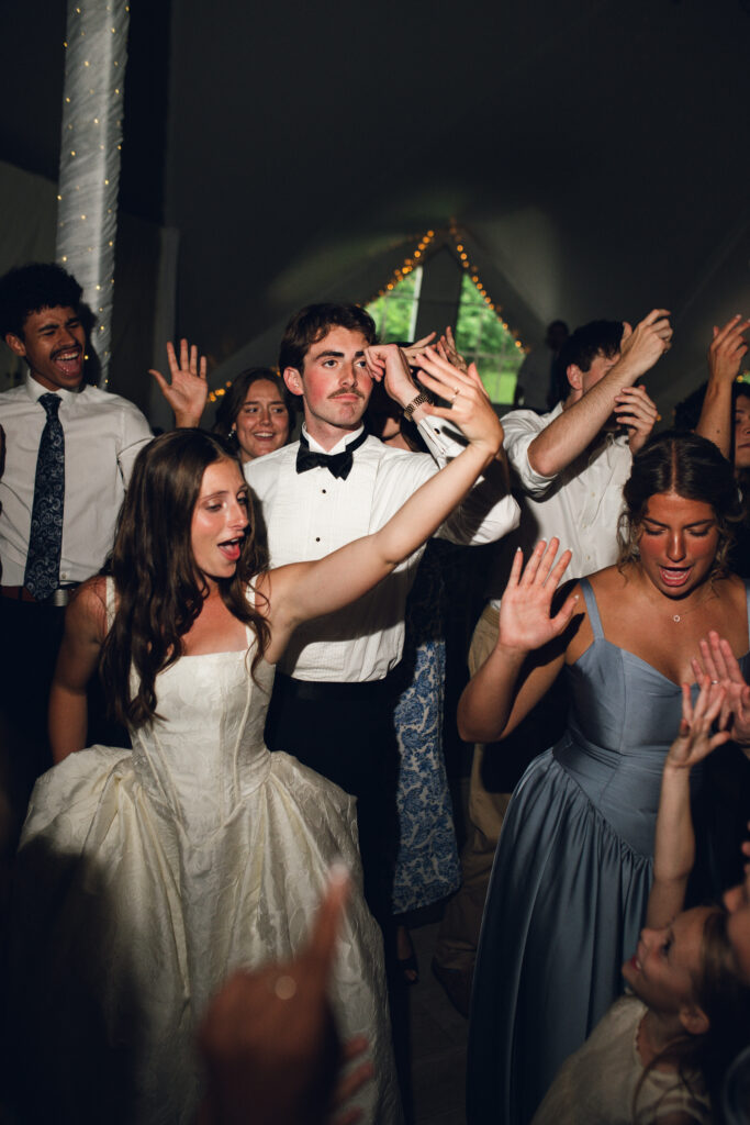The bride, groom, and wedding guests celebrating and dancing together on a packed dance floor at the Longview Mansion reception.