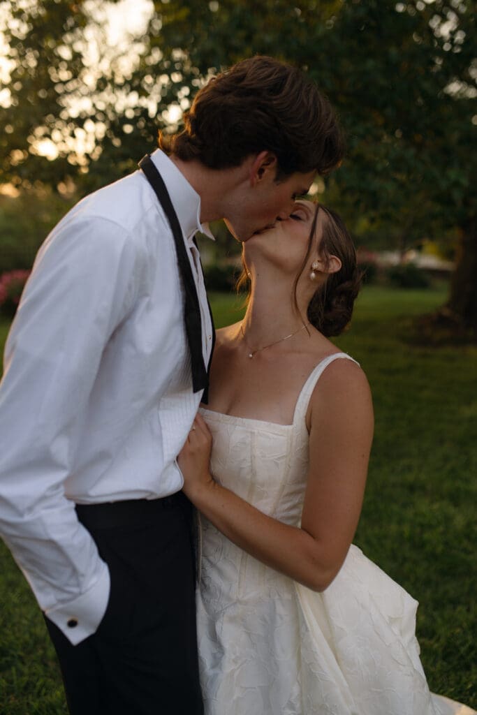 Intimate sunset wedding portrait of the bride and groom kissing each other while standing on the grass grounds of Longview Mansion.