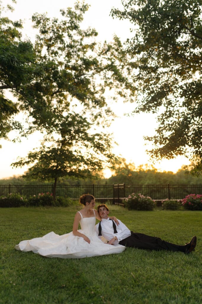 Intimate sunset wedding portrait of the bride and groom looking at each other while resting on the grass grounds of Longview Mansion.
