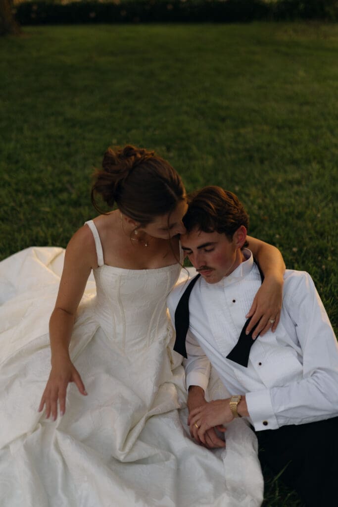 Intimate sunset wedding portrait of the bride and groom looking at each other while resting on the grass grounds of Longview Mansion.